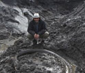 scientist standing next to outcrop containing a mammoth tusk.