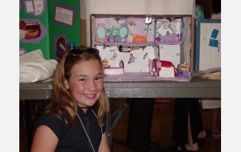 Young girl smiles at camera, science project in background.