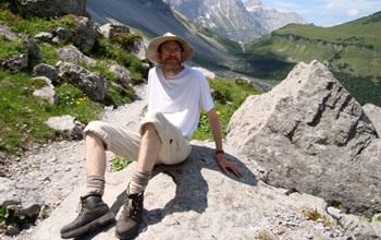 Photo of Thomas DeGrand sitting on a rock in a scenic, mountainous area