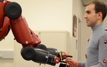 Photo of a man handing ethernet cables to 2 robotic arms.