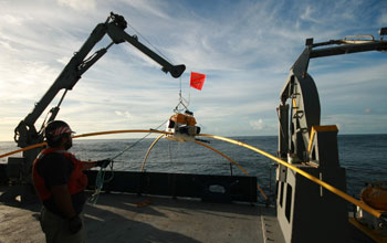 Researcher on a ship pulls a receiver from the ocean using a crane