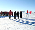 A memorial ceremony at South pole showing people gathered on the ice and the Canadian flag.