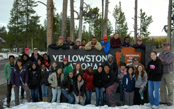 Photo of people gathered around sign Yellowstone National Park with the National Park Service logo.