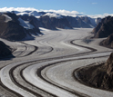 Photo of a glacer with mountains on both sides and trails of rock and soil in the glacier.