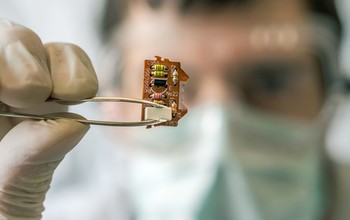 A scientist holds an electronic circuit with a set of tweezers.