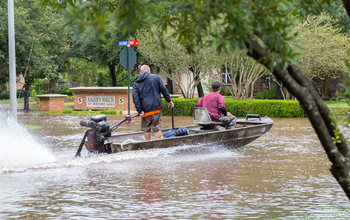 Two men in motorboat traveling along flood-covered street.