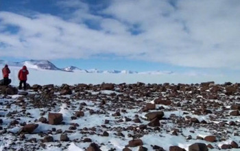 Two researchers and rocks, ice, distant mountains in Antarctica