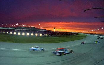 Several race cars rounding a turn at a racetrack at sunset