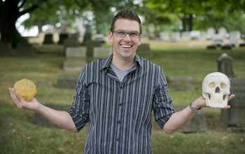 Timothy Verstynen in graveyard holding a plastic skull and brain.