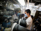 A man in a lab working on something behind a protective glass shield.