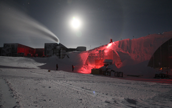South Pole employees remove snow from the top of buildings during the winter darkness