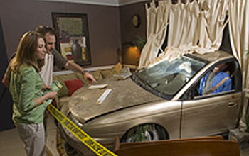 Photo of two guests observing a crime scene exhibit featuring a car that collided with a house
