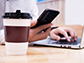 a person on a laptop and cellphone with a cup of coffee