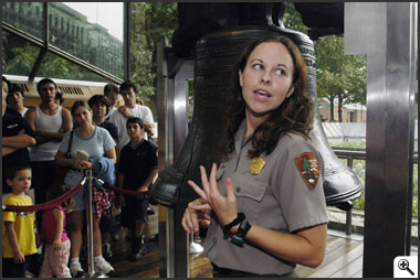 Park ranger in talking to audience in front of bell -- Click to enlarge