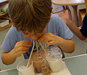Boy blowing using 3 straws to blow bubbles in 3 glasses